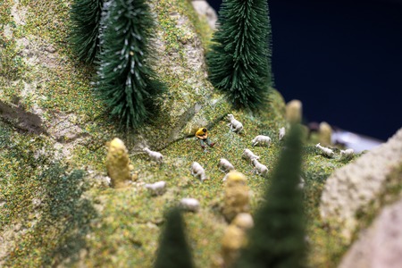 Miniature people: young shepherd reading a book and sheeps walking around him on the green grass of the lawn. Macro photo, shallow DOFの写真素材