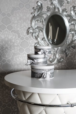 Three round celebration gift boxes with silver ribbon bows on white table. Stack of presents in...
