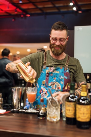 KIEV, UKRAINE - 30 OCTOBER, 2016: Barman festival. Handsome bearded hipster barman with long beard and mustache with funny face holding shaker and making alcoholic cocktailのeditorial素材