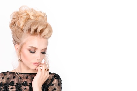 Beautiful blonde woman in elegant black evening dress with updo hairstyle. Her eyes is closed showing bright makeup. Free space for text. Fashion advertising photoの写真素材