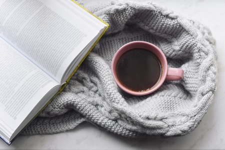 Cozy home still life: cup of hot coffee and opened book with warm plaid on windowsill against snow landscape outside. Winter holidays, Christmas time concept, free copy spaceの写真素材