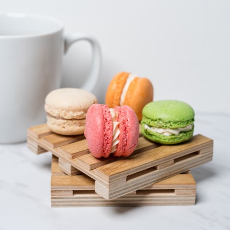 Sweet and colourful macaroons served on little wooden pallets with cup of coffee on a marble texture background. Traditional french dessert.の写真素材