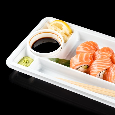 Sushi rolls made of fresh raw salmon, cream cheese and avocado in white plastic container ready to eat on black background with reflections.の写真素材