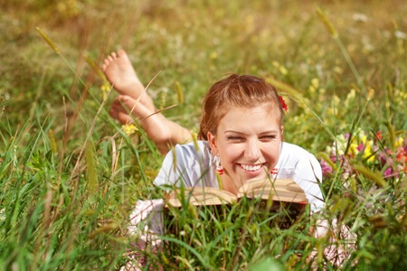 Beautiful young woman-student reading a book lying on the grass. Pretty girl outdoors in summertimeの写真素材