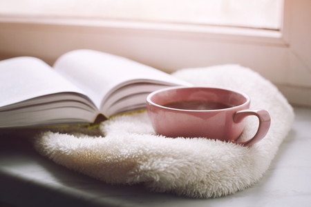 Cozy home still life: cup of hot coffee and opened book with warm plaid on windowsill against snow. Free copy spaceの写真素材