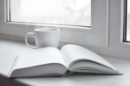 Cozy home still life: cup of hot coffee or tea and opened book on windowsill. Education concept, free copy spaceの写真素材