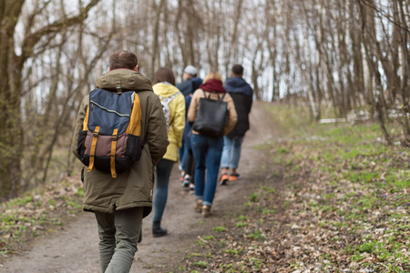 Group of friends walking with backpacks in spring forest from back. Backpackers hiking in the woods. Adventure, travel, tourism, active rest, hike and people friendship concept.の写真素材