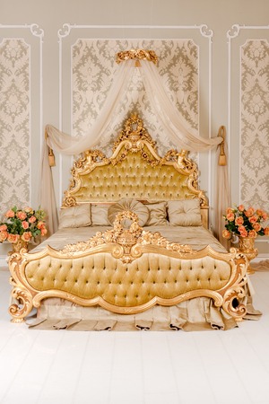 Luxury bedroom in light colors with golden furniture details. Big comfortable double royal bed in elegant classic interiorの写真素材