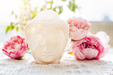 Buddha face. Buddha statue made of white marble with flowers. Concept of peace, calm and tranquility. Buddhist artifact for Zen style interior decor.の写真素材