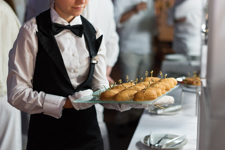 Catering service. Waiter carrying a tray of appetizers. Outdoor party with finger food, mini burgers, sliders.の写真素材