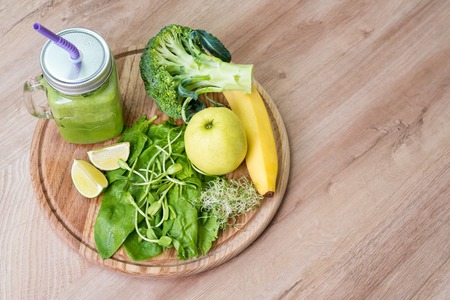Fresh green vegetables and green smoothie in jar. Detox, diet or healthy food concept. Mason jar of dietary drink with broccoli, spinach, microgreens, lime and banana on wooden background. Top view.の写真素材