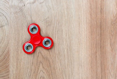 Fidget spinner. Red hand spinner on wooden background. Free space for text.の写真素材