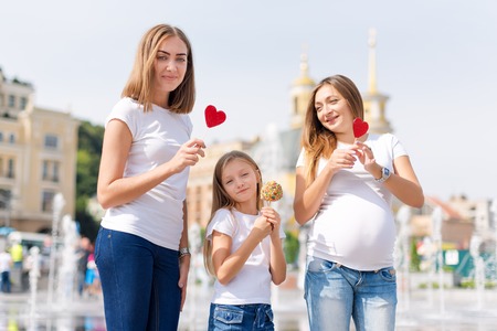 Same sex lesbian family with child on a walk in the park near the fountains. Lesbians mothers with adopted child, happy family, pregnant couple with kid.の写真素材