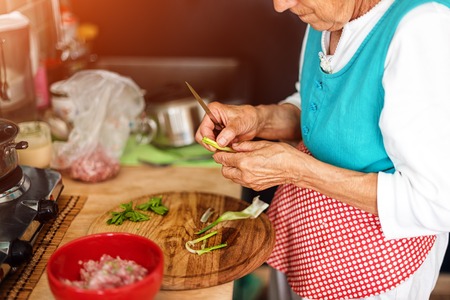 Senior woman hands chopping vegetables on a wooden board in the kitchen.の写真素材