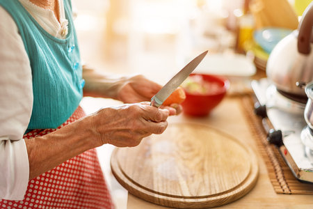 Senior woman hands chopping vegetables on a wooden board in the kitchen.の写真素材