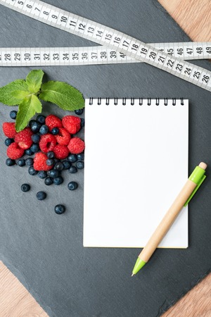 Blueberries, raspberries, mint, measuring tape and notepad for writing notes or resolutions, concept of sport, diet, slimming, detox, healthy lifestyles and nutrition. Mock up, space for text.の写真素材