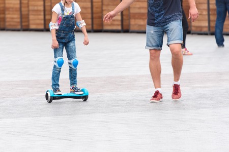Little girl riding a hoverboard on the city square. New movement and transport technologies. Dual wheel self balancing electric skateboard. People on electrical scooter outdoors.の写真素材