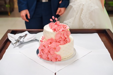Bride and groom cutting their wedding cake decorated with orchids.の写真素材