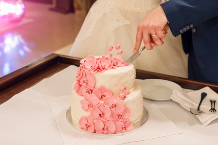 Bride and groom cutting their wedding cake decorated with orchids.の写真素材