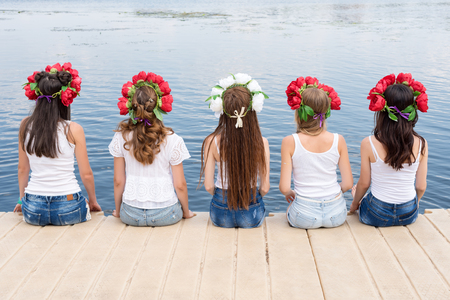 Back view of five young ladies, wearing flower wreaths, jeans and white tshirts. Group of friends sitting on the side of the pool or on pier. Pool party, summer vacation. Banner for website.の写真素材
