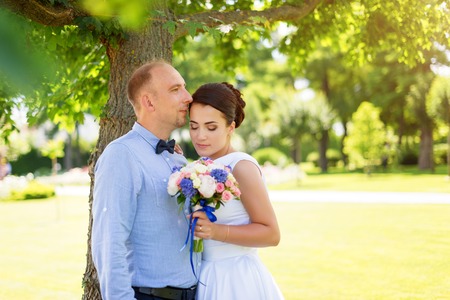 Bride and groom kissing outdoors. Wedding day of happy bridal couple, newlywed woman and man embracing with love in the park.の写真素材
