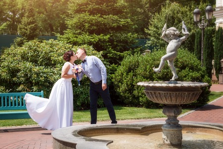 Bride and groom kissing outdoors. Wedding day of happy bridal couple, newlywed woman and man embracing with love in the park.の写真素材