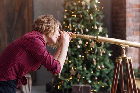 Woman in decorated living room for christmas is looking at the window with spyglass. Looking forward to a new year.の写真素材