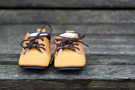 Yellow baby boots close up. Kid shoes on wooden bench in the park.の写真素材