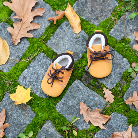Baby boots in autumn park. Kid shoes with yellow leaves outdoors.の写真素材