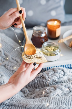 Female hands smearing cream cheese on fresh bread. Breakfast in bed, a tray with cheese, grissini, jam and aromatic candle. Christmas morning. Honeymoon. Early morning at the hotelの写真素材