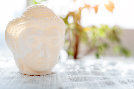 Buddha face. Buddha statue made of white marble with flowers. Concept of peace, meditation, calm and tranquility. Buddhist artifact for Zen style interior decor.の写真素材