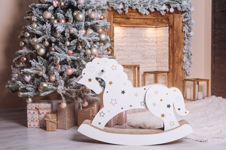 Beautiful holiday decorated room with Christmas tree, wooden horse and presents near the fireplaceの写真素材