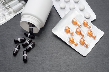 Supplement capsules are poured from white bottle, tablets and ampoules on slate board. Top view. Medicine theme, health care conceptの写真素材