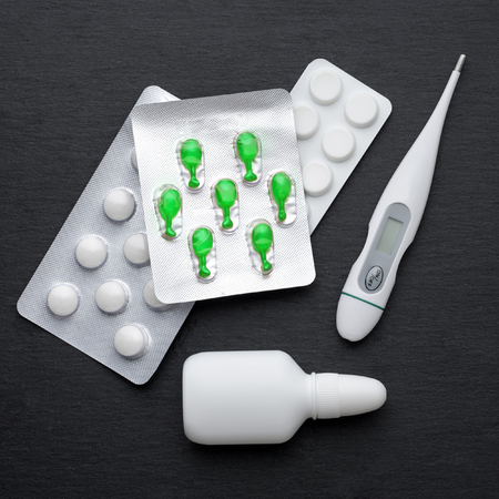 Thermometer, nasal drops and tablets on dark slate board. Flat lay. Meds for flue treatment, health...