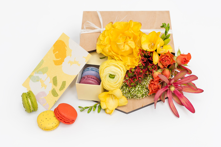 Giftbox with flowers and sweets. Macaroons and spring bouquet in wooden box on white background.の写真素材