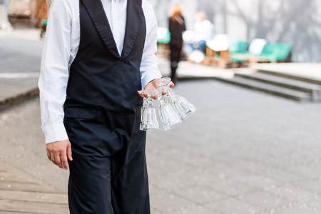 Waiter holding empty glasses outdoors, no face, closeup.の写真素材