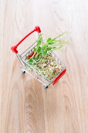Micro greens in shopping cart on wooden background. Different types of microgreens for sale. Healthy eating concept of fresh garden produce organically grown, symbol of health. Vitamins from nature.の写真素材