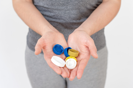 Female hand holding plastic bottle caps. Two hands with plastic lids. Recyclable waste. Recycling, reuse, garbage disposal, resources, environment and ecology concept.の写真素材