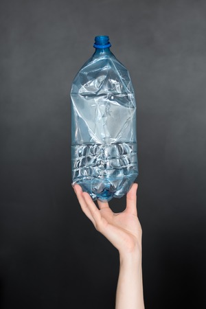 Female hand holding empty crushed plastic bottle isolated on black background. Recyclable waste. Recycling, reuse, garbage disposal, resources, environment and ecology conceptの写真素材