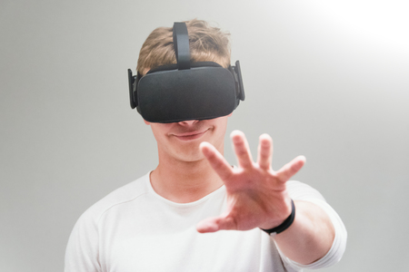 Man wearing virtual reality goggles on gray background. Student using VR headset.