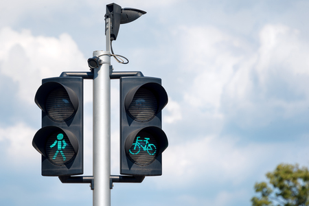 Green bicycle and pedestrian traffic lights. Green traffic light for bikes, gives cyclists priority, pedestrians crossing traffic lights with city backgroundの写真素材