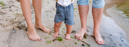 Happy family on the beach. Closeup of feet of family with little baby boy walking on sand. Man and...