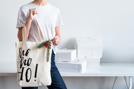 Unrecognizable woman holding Christmas gift in cloth bag. Happy winter holidays. Presents for Christmastime celebrationの写真素材