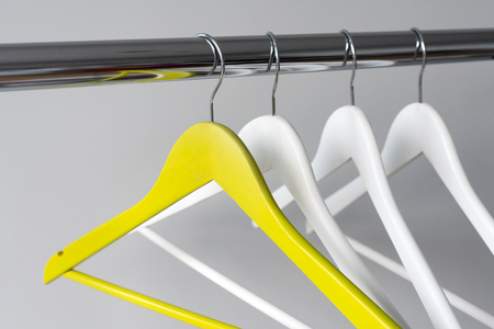 Empty clothes hangers on metal rail against grey background. Rectangular metal clothing rail with empty color wooden coat hangers.の写真素材