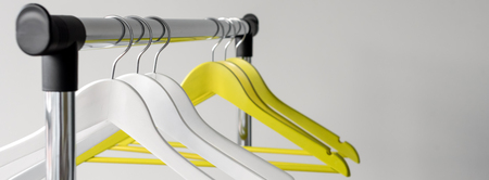 Empty clothes hangers on metal rail against grey background. Rectangular metal clothing rail with empty color wooden coat hangers.の写真素材