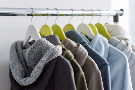 Hanger stand with spring or autumn warm clothes on grey background. Cold season, cozy sweaters and hoodie on hangersの写真素材