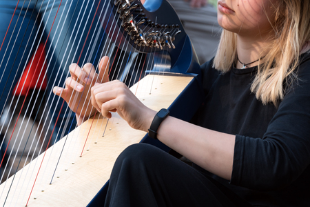 Closeup of a beautiful girl playing the harp. Detail of a woman playing the harp outdoorsの写真素材