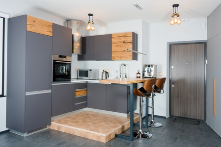 Modern kitchen interior with lights on. Brown wooden table and bar stools, coffee machine....