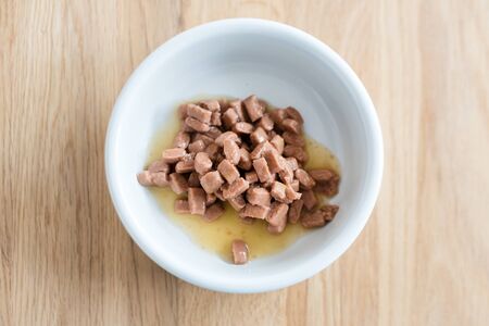 Wet food for cats and dogs in a white bowl on wooden floor close upの写真素材