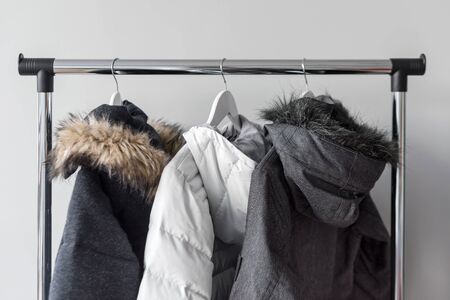 Hanger stand with warm jackets. Winter jackets with fur collar hang on white wooden hangers. Collection of winter jackets in shop. Winter season fashion backgroundの写真素材